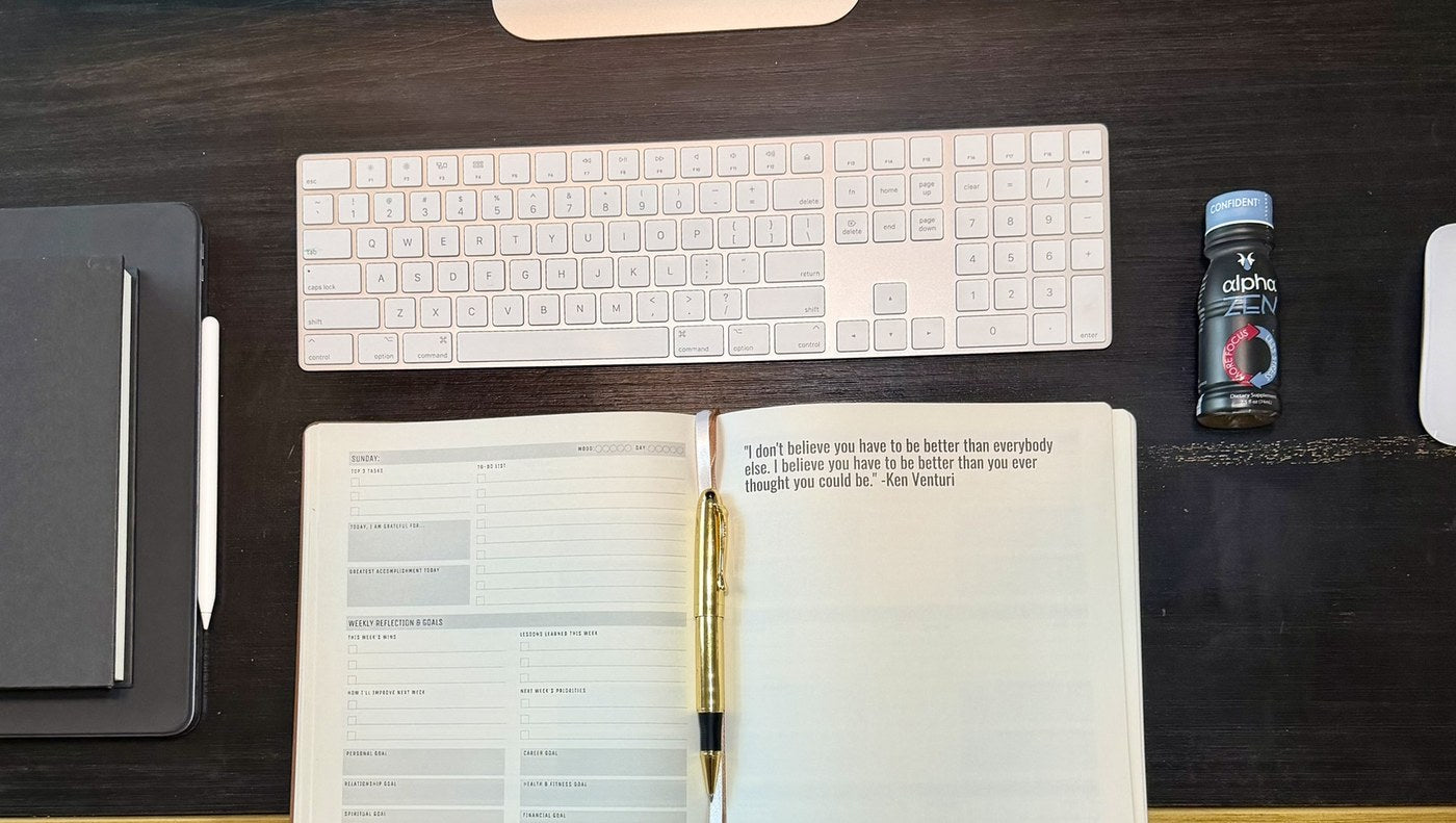 A desk with an open journal, a keyboard and an Alpha Zen shot, ready for the first entry